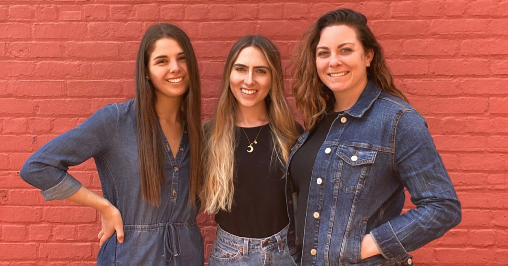 three white women in their 20s in front of a brick wall